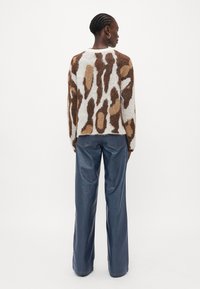 Brown and beige patterned knit sweater with a loose fit, worn over high-waisted dark denim jeans, featuring straight, wide legs.