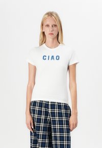 Hvit bomulls t-skjorte med blå, fluffy "CIAO"-tekst på forsiden. Korte ermer og rund hals, sammen med bukser i blå og svart rutete mønster.