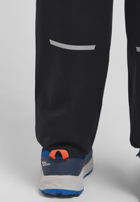 Pantalons de sport noirs avec des accents réfléchissants, associés à des chaussures bleu et gris avec un onglet de talon orange et une tige en maille texturée.