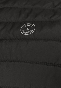 Schwarze gepolsterte Jacke mit einem gesteppten Muster und einem kreisförmigen weißen Logo, in dessen Mittelpunkt "JACK & JONES" gestickt ist.