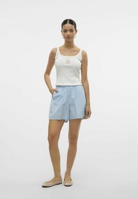 Witte tanktop met vierkante halslijn en schelpenafbeelding, gecombineerd met blauwe gestreepte shorts met elastische tailleband en zijzakken. Platte beige schoenen.