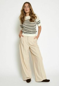 Maglione a maglia con strisce bianche, blu navy e nere; pantaloni larghi crema; texture liscia; vestibilità comoda; tasche laterali; abbinati a calzature marroni.