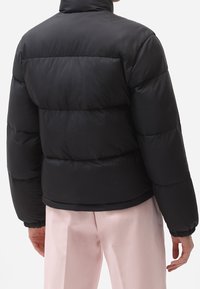 Czarna kurtka puchowa z wysokim kołnierzem, z pikowanym wzorem, grubym wypełnieniem i elastycznymi mankietami w połączeniu z gładkimi różowymi spodniami.