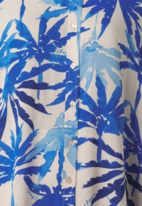 Blue and white button-up shirt featuring a tropical leaf pattern, light fabric, and round buttons with a smooth texture.