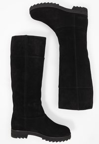 Černé semišové kozačky po kolena s plochou gumovou podrážkou, které mají hladký povrch a minimální detaily šití. Navrženo pro těsnou přiléhavost.