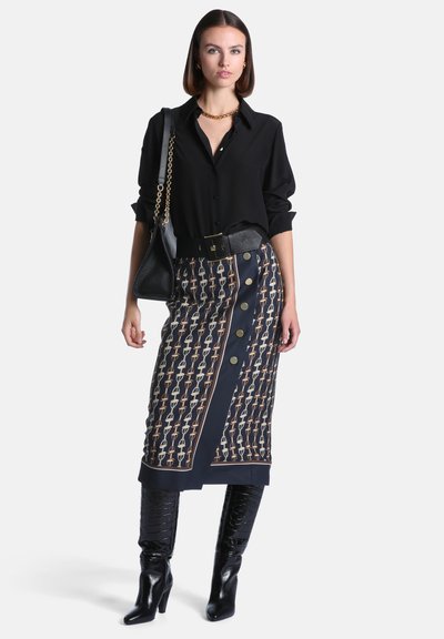Femme portant une blouse noire, une jupe midi à motifs avec de gros boutons, une ceinture noire, des bottes noires montantes et un sac à main noir à bandoulière chaîne dorée.