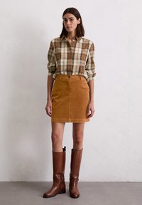 Bruine geruite overhemds, een tan kleurige corduroy rok en kniehoge bruin leren laarzen. Gladde textuur, getailleerd ontwerp en zichtbare stikdetails.