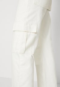 Vita cargobyxor med lös passform, som har stora sidofickor, tillverkade av slitstark bomull, med synliga sömmar.