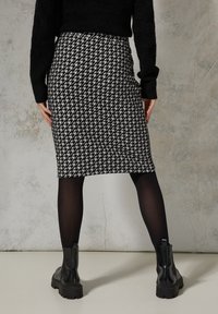 Schwarzer und weißer Hahnentritt Bleistiftrock in taillierter Passform, kombiniert mit schwarzen Strumpfhosen und klobigen schwarzen Ankle Boots.