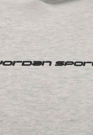 Κείμενο «jordan sport» με μαύρη μοντέρνα γραμματοσειρά σε φόντο από ανοιχτό γκρι ύφασμα.