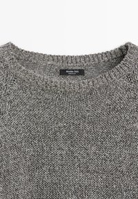 Gros plan sur l'encolure d'un pull gris en tricot avec une étiquette noire affichant "Massimo Dutti Made in Italy."
