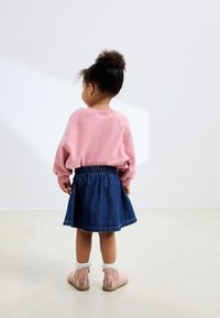 Pinkfarbenes langärmeliges Sweatshirt, Jeansrock, pinke Stiefel mit Blumenstickerei und Spitzenakzenten, lockiges Haar zu einem Dutt gebunden. Rückansicht.