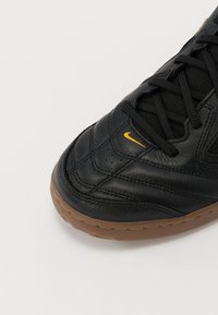 Čierne kožené tenisky s textúrovaným povrchom, žltým Nike swooshom, čiernymi šnúrokami a hnedou gumovou podrážkou, s prešitou detalizáciou.