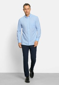 Camicia azzurro chiaro con maniche lunghe e taschino sul petto, abbinata a pantaloni navy scuri e scarpe eleganti nere. Tessuto di texture liscia.