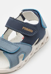Sandalo in velcro blu e grigio con upper testurizzato, suola in gomma bianca e caviglia imbottita. Presenta il logo "Primigi" in oro.