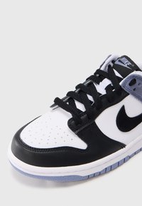 Musta-valkoinen lenkkari, jossa on nahka- ja verkkomateriaaleja, rei'itetty kärki, mustat nauhat ja vaaleansininen kumipohja.