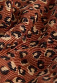 Leopardenmusterstoff mit einer strukturierten, gerippten Oberfläche in Rost-, Creme- und Schwarztönen. Die Muster zeigen unregelmäßige Fleckenformen.