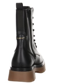 Stivaletto in pelle nera con cerniera laterale, pannello elastico, punta tonda e suola marrone spessa. Presenta un dettaglio del logo sul tallone.