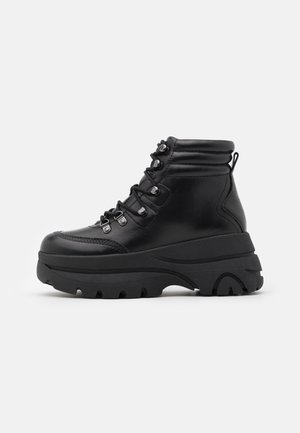 Bottines noires en cuir lisse, dotées d'une semelle épaisse texturée et d'une fermeture à lacets avec œillets métalliques et boucle arrière.