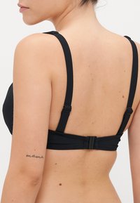Juodas bikini viršus su plačiomis petnešomis ir saugiu užsegimu nugaroje. Lygi tekstūra, struktūruota dizainas, minimalistinis stilius.