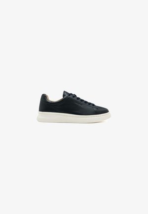 Sneaker en cuir noir avec une texture lisse, semelle en caoutchouc blanche, bout rond et œillets en métal pour les lacets. Design minimaliste.