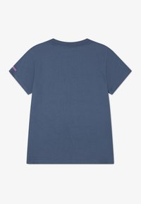 Krátký rukáv, modré bavlněné tričko s kulatým výstřihem. Na levém rukávu je růžový nápis. Hladký materiál a volný střih.