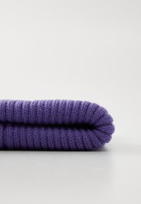 Lilla strikket stoff, rullet sammen, som viser et strukturert mønster med ribbestrikkedetaljer og en myk, plysjaktig utseende.