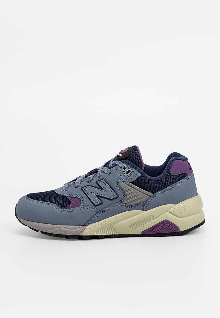 Zapatilla deportiva gris y marina con material de malla y ante, que presenta un acento púrpura, una entresuela texturizada y una suela de goma.