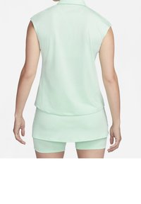Femme portant un haut sans manches vert menthe et un short assorti, debout de dos devant un fond blanc.