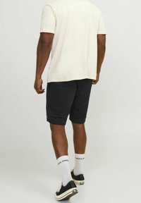 T-shirt blanc à manches courtes et short noir. Le t-shirt est uni ; le short a une taille élastique et des poches latérales. Baskets noires et chaussettes blanches.