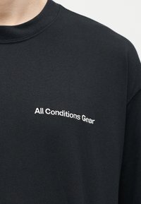Μαύρο μπλουζάκι με στρογγυλή λαιμόκοψη και λευκό κεντημένο κείμενο "All Conditions Gear" στην αριστερή περιοχή του στήθους.