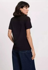 Czarna koszulka z krótkim rękawem, okrągłym dekoltem, gładka w dotyku, dopasowana stylowo, noszona z szerokimi spodniami w kolorze granatowym o wysokim stanie. Niewielki tatuaż widoczny.