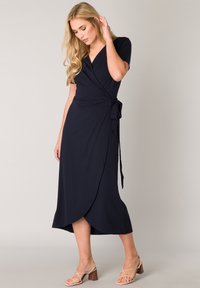 Marineblaues Wickelkleid mit kurzen Ärmeln, tailliertem Bund und einem fließenden Rock, der bis zur Mitte der Waden reicht. Glattes Material ohne sichtbare Muster.