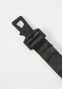Juodas nailono diržas su plastikiniu užsegimu, pasižymintis lygiu paviršiumi ir saugiu užsegimo mechanizmu tvirtinimui. Paprastas ir funkcionalus dizainas.