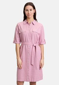 Jasno-różowa, do kolan sukienka z lnu, z przodem na guziki, kołnierzykiem, dwiema kieszeniami na piersi i materiałowym paskiem. Krótkie rękawy.
