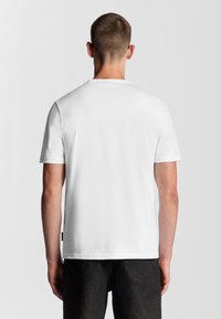 Camiseta de algodón blanca con mangas cortas y cuello redondo. Textura suave, diseño sencillo y una pequeña etiqueta en el lado inferior.