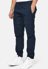 Pantalones de chándal azul marino con cintura y puños elásticos. Incluye varios bolsillos tipo cargo y un bolsillo lateral con cremallera. Fabricados con un tejido duradero.