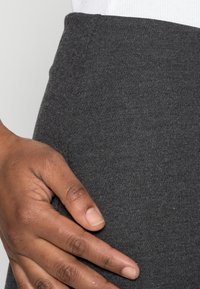 Tessuto grigio scuro testurizzato di un girovita aderente, con una mano appoggiata di lato, che mostra la morbidezza e l'elasticità del tessuto.