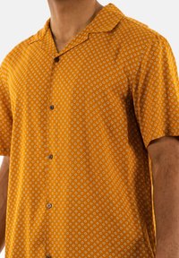 Korte mouwen shirt van mosterdgele stof met een subtiel ruitpatroon, voorzien van een klassieke kraag en donkere knopen.