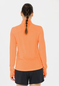 Lyst orange langærmet atletisk top med en tætsiddende pasform og tekstureret stof, parret med sorte atletiske shorts.