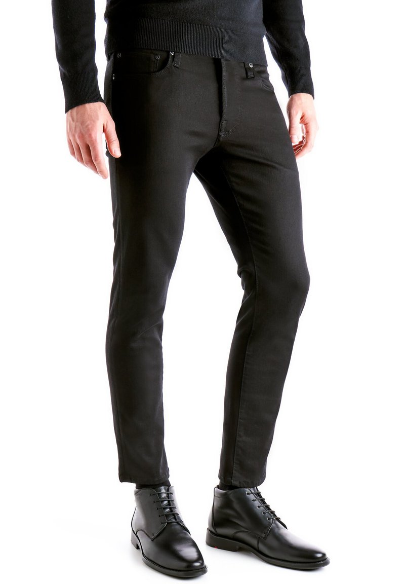 Jeans noirs à coupe ajustée, en denim, avec poches avant et fermeture éclair. Portés avec des bottes noires à lacets pour un look soigné.
