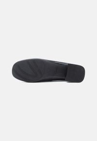Sola de um sapato formal preto com um salto quadrado e uma pega de borracha texturizada, mostrando o logótipo da marca perto da área do mediopié.