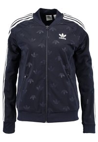 Marinblå zip-jacka gjord av slät tyg, med vita ränder på ärmarna och ett subtilt mönster av logotyp-siluetter. Elastiska muddar och nedkant.