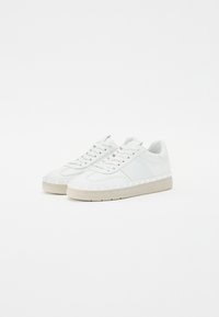 Baskets en cuir blanc avec une finition lisse, des accents texturés et une semelle en caoutchouc beige clair. Elles possèdent des lacets plats et des détails cousus.