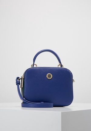 Kleine gestructureerde blauwe leren handtas met een bovenhandvat, afneembare schouderriem en een rond gouden logo-embleem aan de voorkant.