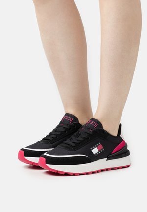 Schwarze Sportschuhe mit rosa Akzenten, die ein Design aus gemischten Materialien aufweisen, eine kontrastierende weiße Sohle haben und ein markiertes Detail an der Seite besitzen.