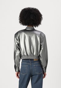 Metalna srebrna bomber jakna z oprijetim pasom, rebrastim ovratnikom in gladko teksturo. Kombinirana z modrimi jeans hlačami z visokim pasom.