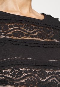 Schwarzes Top mit geschichteter Spitze und strukturiertem Stoff. Intricate blumige Muster mit gezackten Kanten. Leichter und transparenter Material.