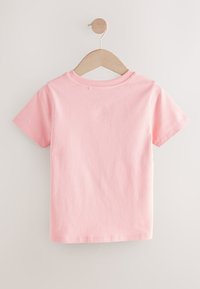 T-shirt rose à manches courtes en coton doux, avec un col rond et une texture lisse. Suspendu à un cintre en bois sur un fond clair.