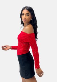 Rød blonde top med off-shoulder og lange ærmer, der har en tætsiddende silhuet og blomster mønstre. Bæres med en sort mini nederdel.